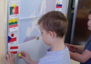 Dzieci mocują flagi krajów europejskich obok mapy Europy na tablicy.